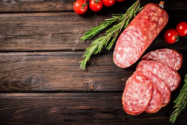 Pieces of delicious salami sausage with rosemary and tomatoes. On a wooden background. High quality photo