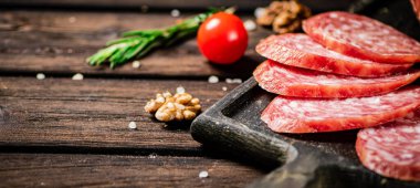 Pieces of salami sausage on a cutting board with cherry tomatoes and rosemary. On a wooden background. High quality photo