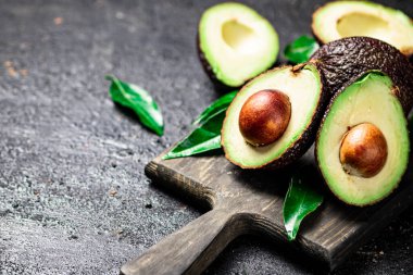 Kesme tahtasında yeşil yapraklı taze avokado. Siyah bir arka planda. Yüksek kalite fotoğraf