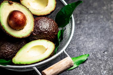 Yarısı ve kevgire batırılmış koca bir avokado. Siyah bir arka planda. Yüksek kalite fotoğraf