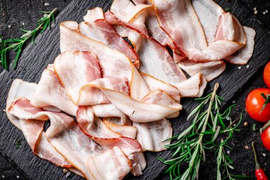 Domatesli ve biberiyeli taş bir tahtanın üzerinde pastırma parçaları. Siyah bir arka planda. Yüksek kalite fotoğraf