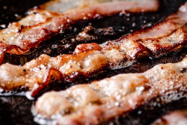 Pieces of bacon are fried in boiling oil with air bubbles. On a black background. High quality photo clipart