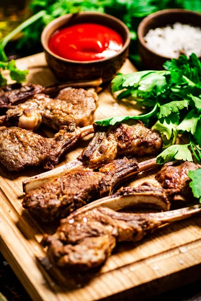 stock image Rack of grilled lamb on a wooden cutting board with parsley. Against a dark background. 