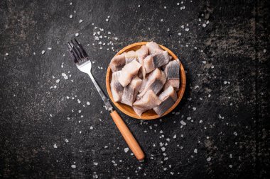 Bir tabak tuz ve çatalla birlikte tuzlanmış ringa balığı dilimleri. Siyah bir arka planda. Yüksek kalite fotoğraf