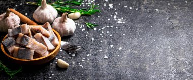 Sarımsak ve biberiyeli ahşap bir tabakta tuzlanmış ringa balığı. Siyah bir arka planda. Yüksek kalite fotoğraf