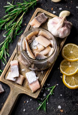 Biberiye ve limonla birlikte kesme tahtasındaki kavanozda tuzlanmış ringa balığı. Siyah bir arka planda. Yüksek kalite fotoğraf