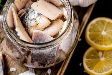 Salted herring in a jar with lemon slices. On a black background. High quality photo clipart