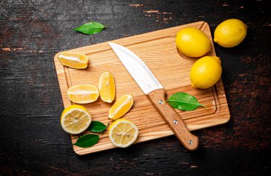 Kesme tahtasındaki limon dilimleri. Bıçak ve yapraklarla. Karanlık bir arka plana karşı. Yüksek kalite fotoğraf
