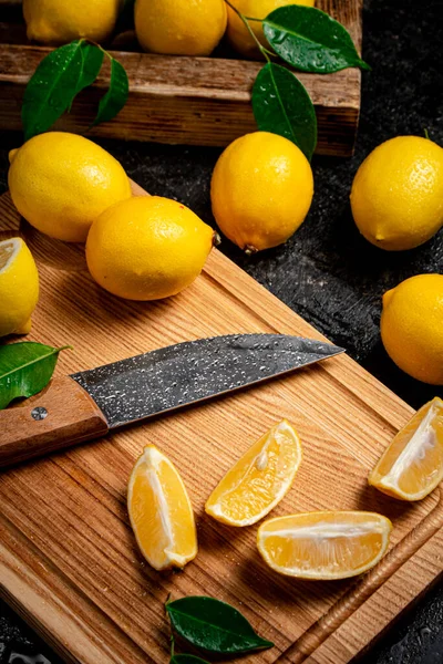 stock image Sliced fresh lemons on a wooden cutting board with a knife. On a black background. High quality photo