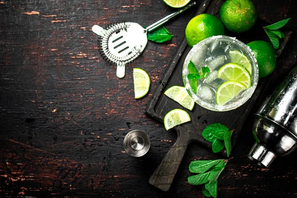 stock image Margarita on a cutting board with pieces of lime and mint leaves. On a rustic dark background. High quality photo