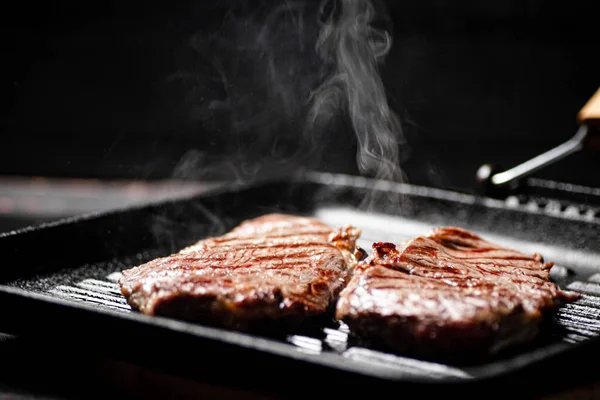 stock image Cooking grilled steak in a frying pan with hot steam. On a black background. High quality photo