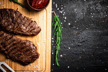 Domates soslu ızgara biftek ve kesme tahtasında biberiye. Siyah bir arka planda. Yüksek kalite fotoğraf