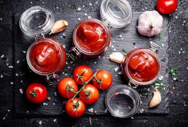 Baharatlı taş bir tahtanın üzerinde cam kavanozlarda domates sosu. Siyah bir arka planda. Yüksek kalite fotoğraf