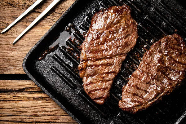Grilled steak in a frying pan. On a wooden background. High quality photo