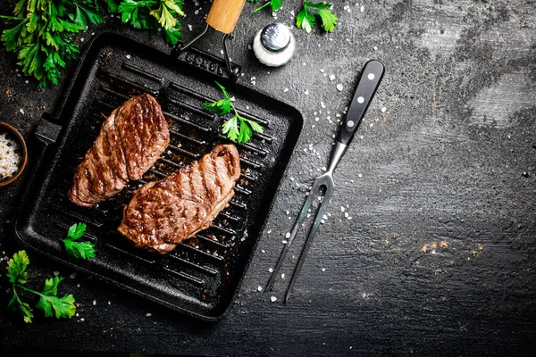 Grilled steak with parsley in a frying pan. On a black background. High quality photo