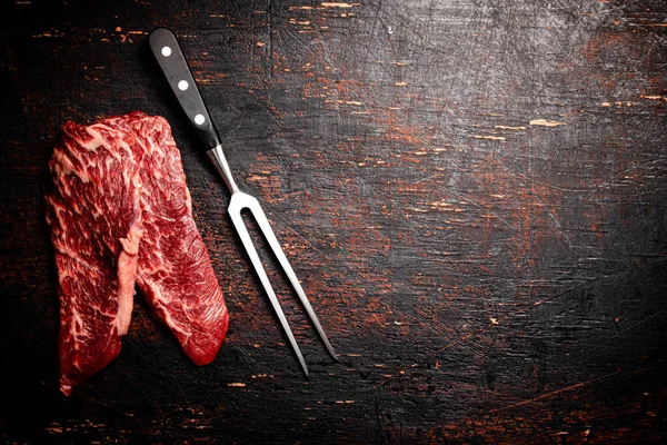 Masada Büyük Bir Çatalla Çiğ Biftek Karanlık Bir Arka Plana — Stok fotoğraf