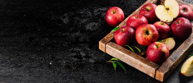Pieces and whole red apples on a wooden tray. On a black background. High quality photo
