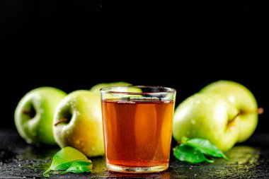 A glass of green apple juice with leaves on the table. On a black background. High quality photo