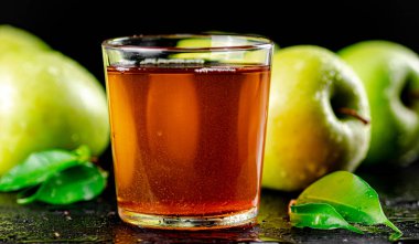 A glass of green apple juice with leaves on the table. On a black background. High quality photo