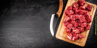 Chopped raw beef on a cutting board with rosemary and a knife. On a black background. High quality photo