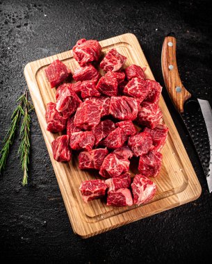 Chopped raw beef on a cutting board with rosemary and a knife. On a black background. High quality photo