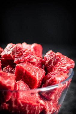 Raw pieces of beef in a glass bowl. On a black background. High quality photo