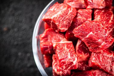 Raw pieces of beef in a glass bowl. On a black background. High quality photo