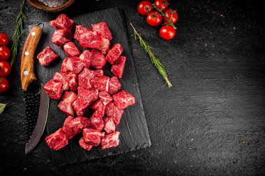 Raw pieces of beef on a stone board with a sprig of rosemary and a knife. On a black background. High quality photo