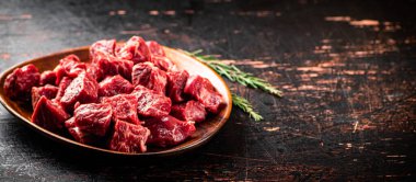 Chunks of fresh raw beef on a plate. On a rustic dark background. High quality photo