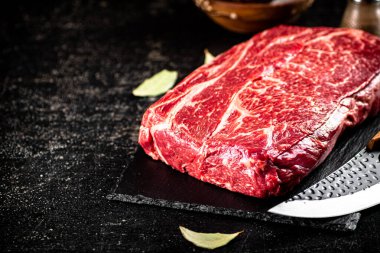 Raw beef on a stone board with a knife. On a black background. High quality photo