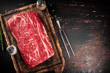 Raw beef on a cutting board with a fork. On a rustic dark background. High quality photo