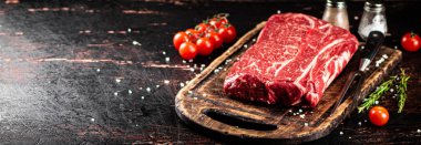 Raw beef on a cutting board with tomatoes. Against a dark background. High quality photo