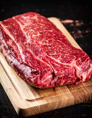 A piece of fresh raw beef on a cutting board. Against a dark background. High quality photo