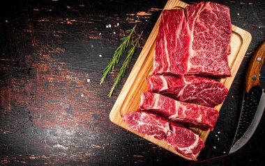 Raw beef on a wooden cutting board with rosemary. On a rustic dark background. High quality photo