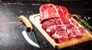Raw beef on a wooden cutting board with rosemary. On a rustic dark background. High quality photo