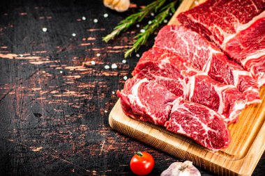 Raw beef on a wooden cutting board with rosemary. On a rustic dark background. High quality photo