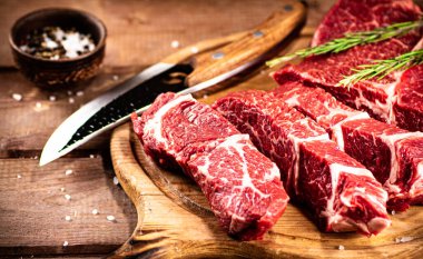 Raw beef on a cutting board with rosemary and spices. On a wooden background. High quality photo