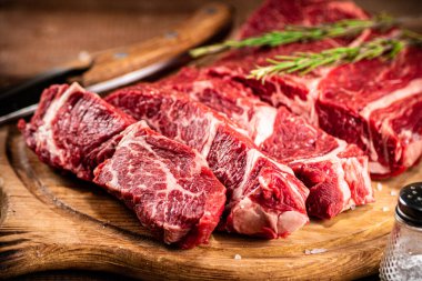Raw beef on a cutting board with rosemary and spices. On a wooden background. High quality photo