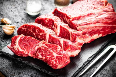 Pieces of raw beef on a stone board. On a black background. High quality photo