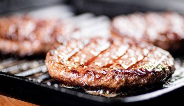 Cooking a delicious grilled burger on a pan with oil bubbles. On a black background. High quality photo