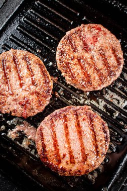 Cooking a delicious grilled burger on a pan with oil bubbles. On a black background. High quality photo