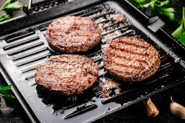 Cooking a delicious grilled burger on a pan with oil bubbles. On a black background. High quality photo