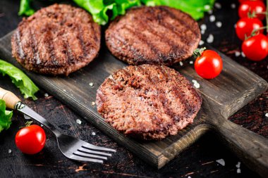Burger grill on a cutting board with tomatoes and greens. On a rustic dark background. High quality photo