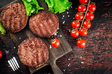 Burger grill on a cutting board with tomatoes and greens. On a rustic dark background. High quality photo