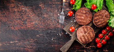 Burger grill on a cutting board with tomatoes and greens. On a rustic dark background. High quality photo
