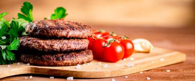Burger grill on a cutting board with greens and tomatoes. On a wooden background. High quality photo