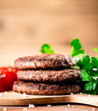 Burger grill on a cutting board with greens and tomatoes. On a wooden background. High quality photo
