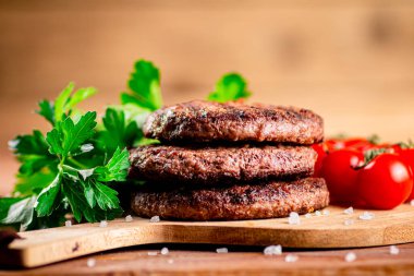 Burger grill on a cutting board with greens and tomatoes. On a wooden background. High quality photo