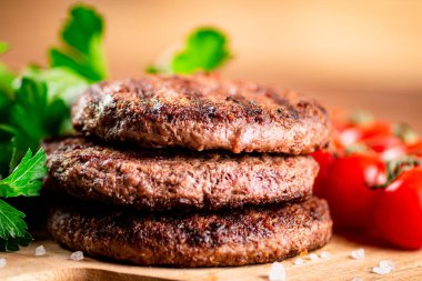 Burger grill on a cutting board with greens and tomatoes. On a wooden background. High quality photo