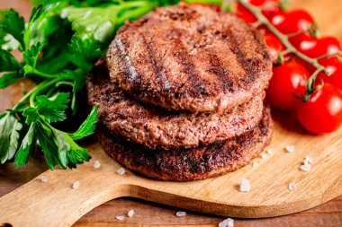 Burger grill on a cutting board with greens and tomatoes. On a wooden background. High quality photo